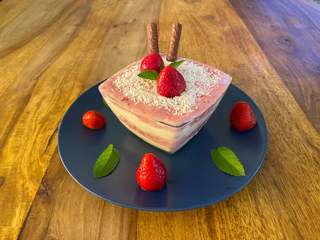 Man sieht die fertige Bowl in einer Glasschüssel, angerichtet auf einem Teller mit Erdbeeren und Minze verziert.