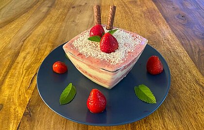 Man sieht die fertige Bowl in einer Glasschüssel, angerichtet auf einem Teller mit Erdbeeren und Minze verziert.