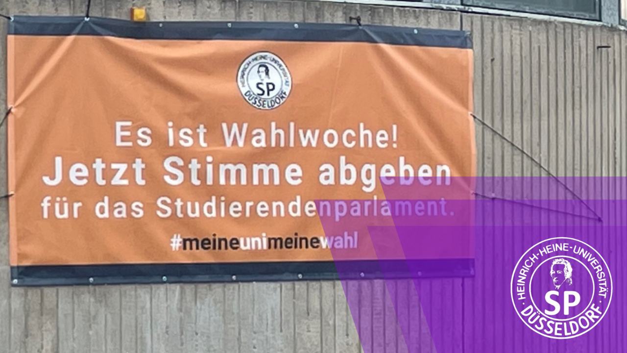 Neben einem großen Banner der Uni machen auch die Listen selbst, mit ihren Ständen auf dem Campus, diese Woche auf die Wahl aufmerksam (Foto: Johanna Beckering) Zu sehen isrt ein Banner, der auf die Wahl aufmerksam macht