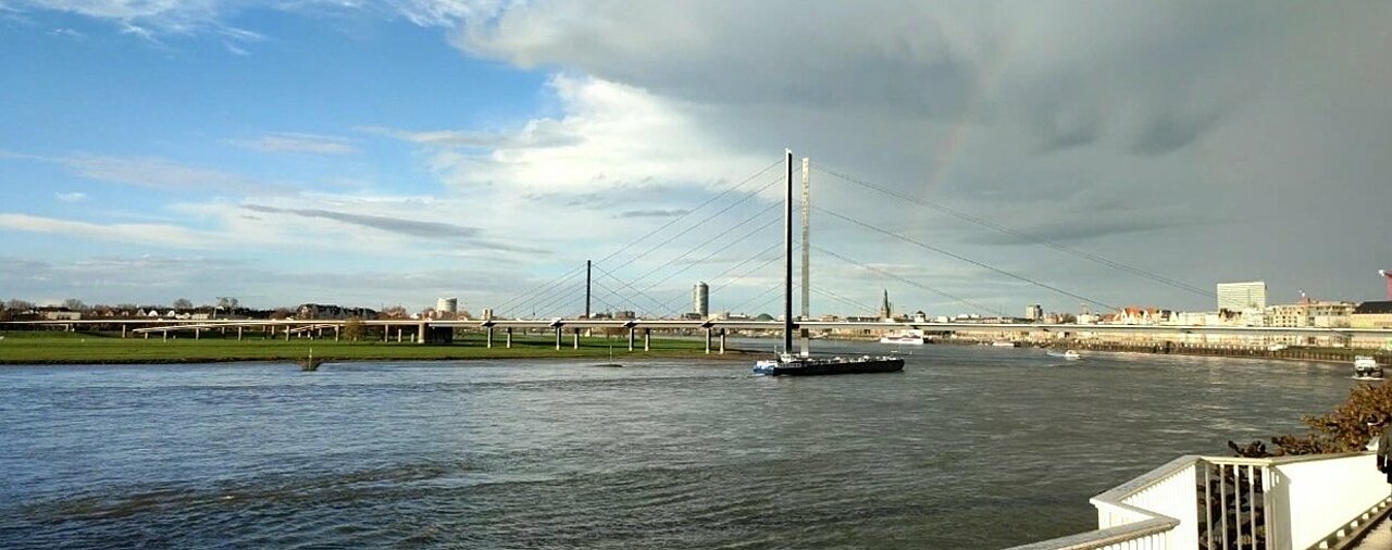 Zu sehen ist der Rhein und ein Regenbogen am Himmel