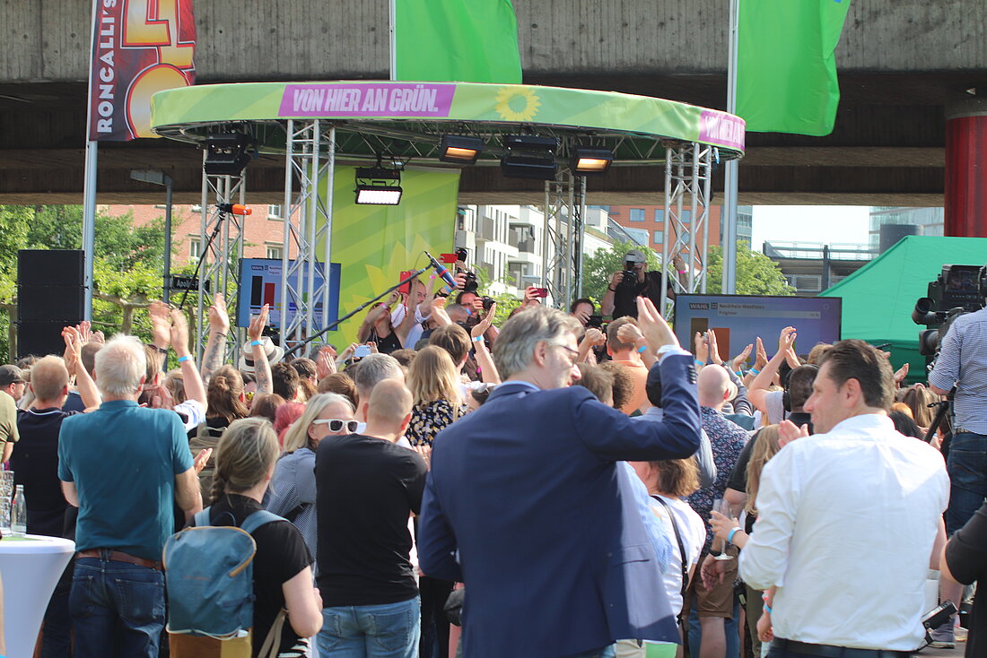 Mitglieder der Grünen klatschen vor einer Bühne, im Freien.