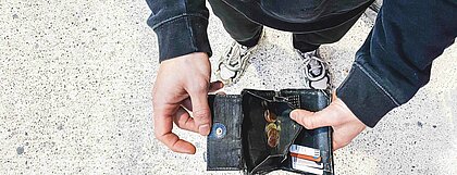 Auf dem Foto sieht man eine Person, die ihren leeren Geldbeutel in die Kamera hält.