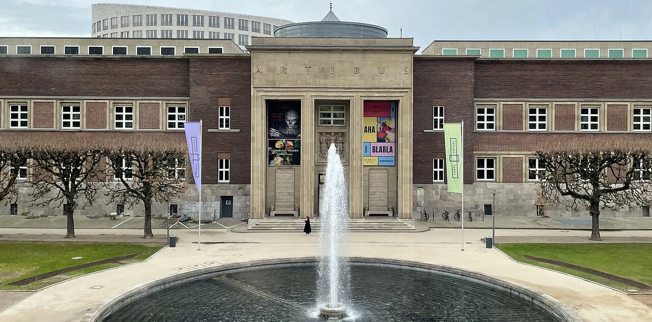 Das Bild zeigt die Eingangsseite des Kunstpalasts in Düsseldorf mit dem großen Springbrunnen davor.