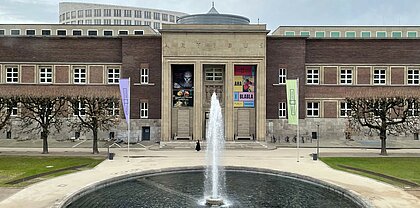 Das Bild zeigt die Eingangsseite des Kunstpalasts in Düsseldorf mit dem großen Springbrunnen davor.