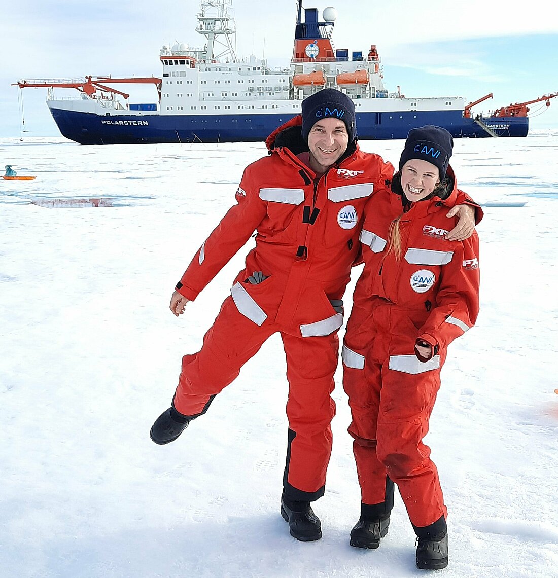 Zu sehen sind zwei Menschen in Schneeanzügen in der Arktis