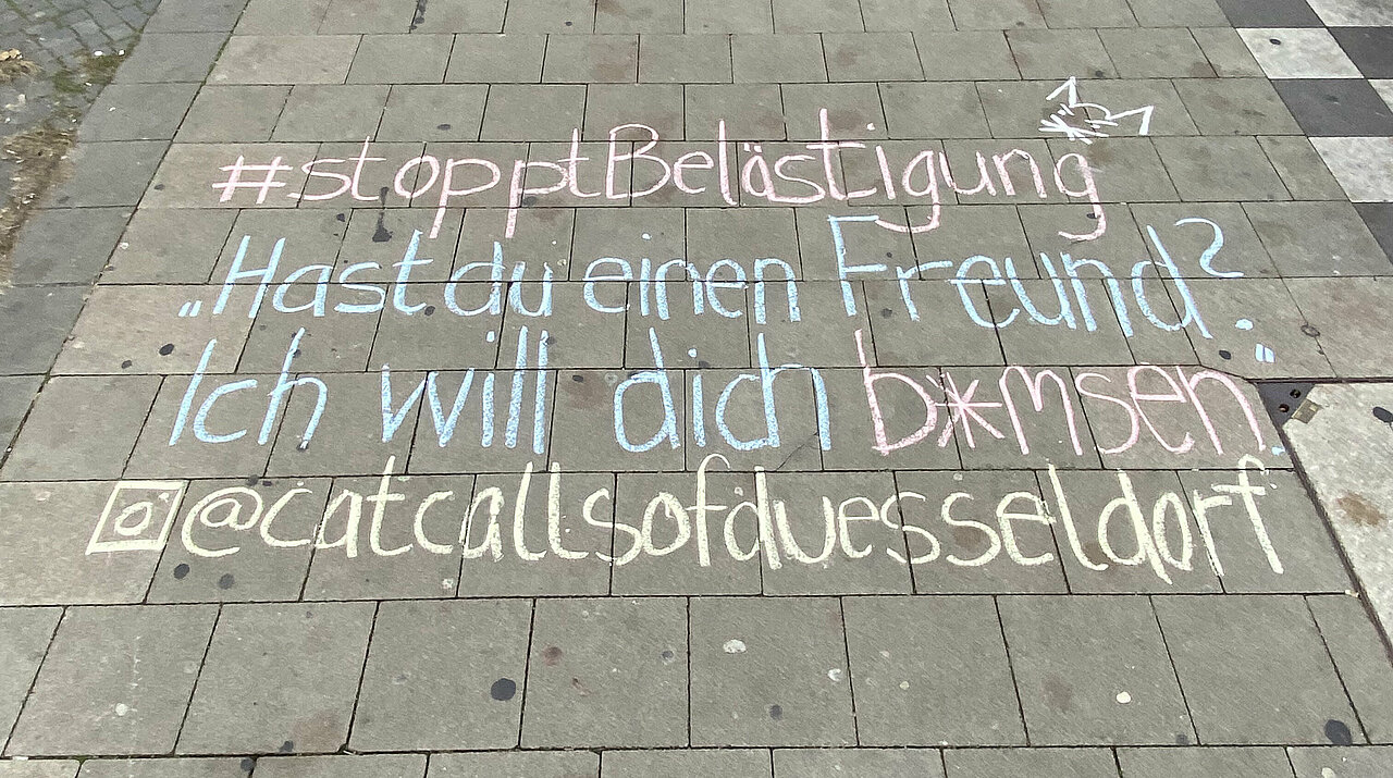 Zu sehen ist Kreide auf der Straße. Es steht geschrieben: #stopptBelästigung "Hast du einen Freund? Ich will dich b*msen" @catcallsofduesseldorf