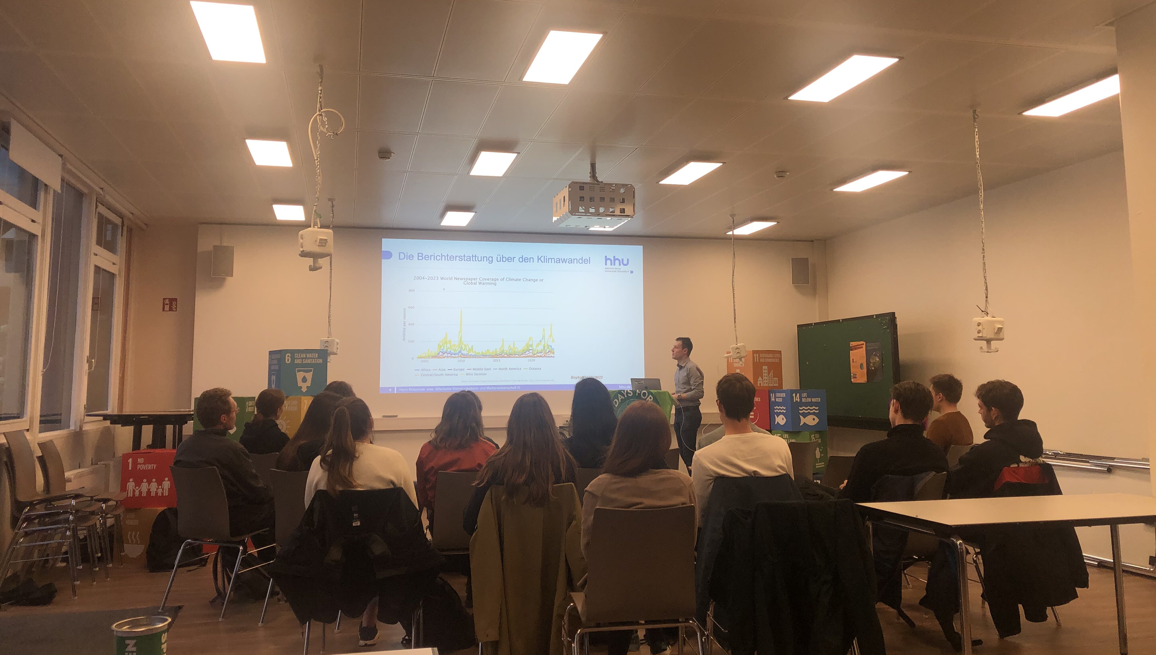 Henri Mütschele sprach während der Public Climate School über Klimakommunikation (Foto: Valeska Ridzewski) Zu sehen ist ein Vortragsraum, in dem eine Gruppe von Menschen stzt und nach vorne blickt