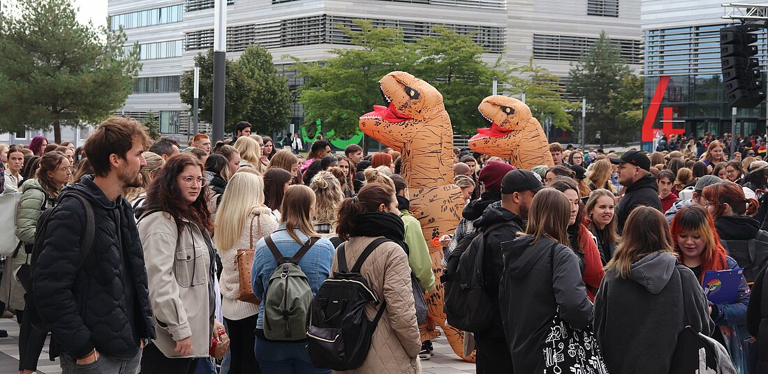 Zu sehen sind viele Erstsemesterstudierende und zwei Menschen in Dinosaurier Kostüm.