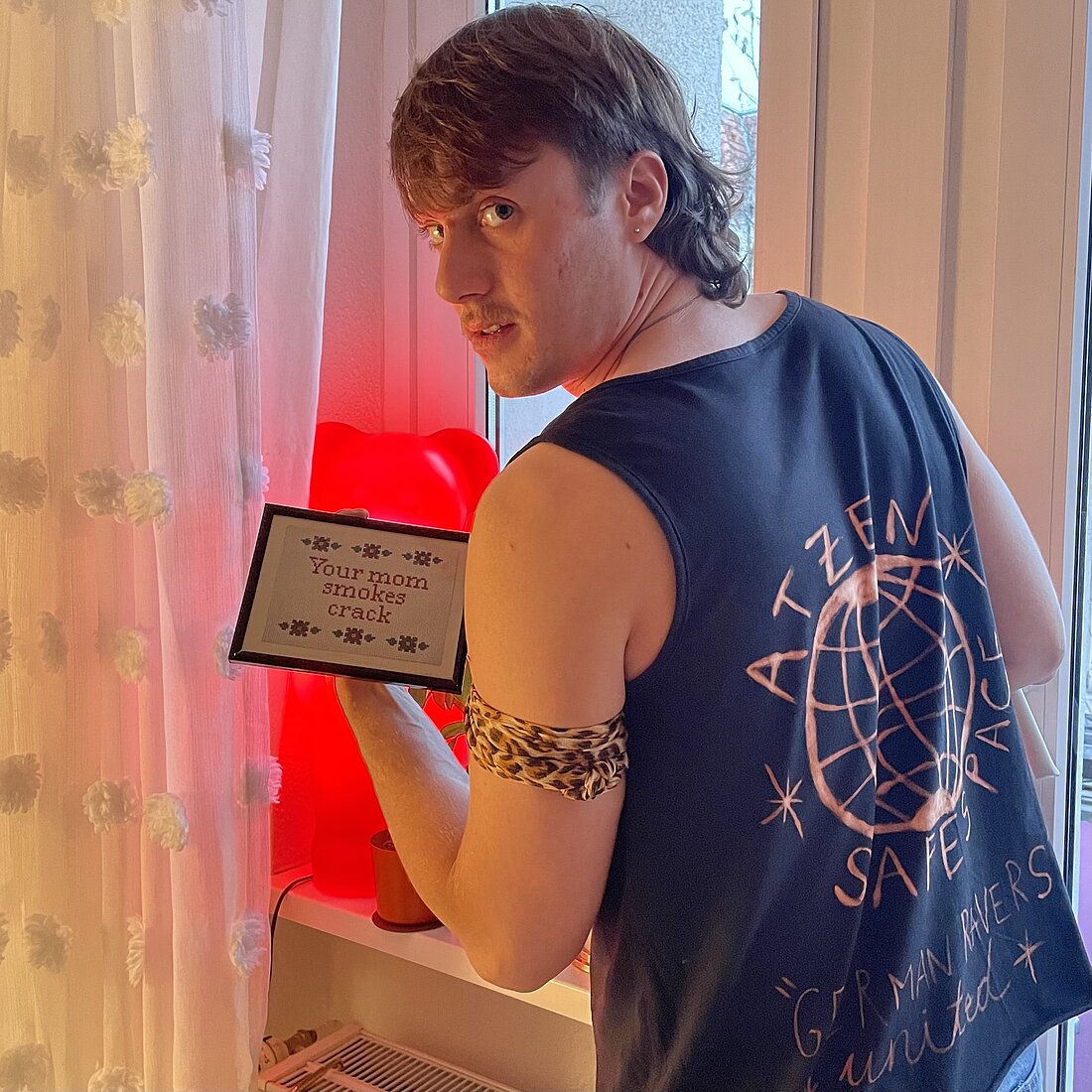 Er bedient den Retro-Techno-Sound: Justin Tinderdate. (Foto: Ramentico) Zu sehen ist ein Pressebild des DJs Justin Tinderdate. Er schaut über die Schulter zur Kamera.