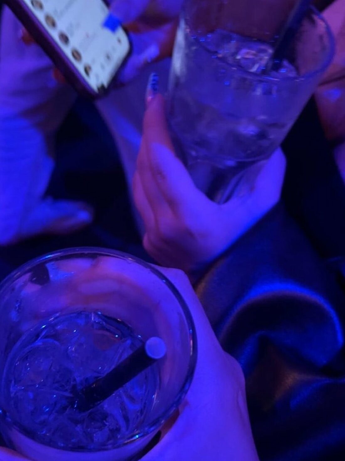 Auf dem Bild sieht man zwei Hände die ein Getränk mit Alkohol halten. Im Hintergrund ist ein geöffnetes Handy mit Snapchat.