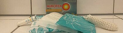 Auf dem Foto sind Binden und Tampons zu sehen. Sie liegen nebeneinander. Dahinter steht eine Verpackung von Schmerztabletten.