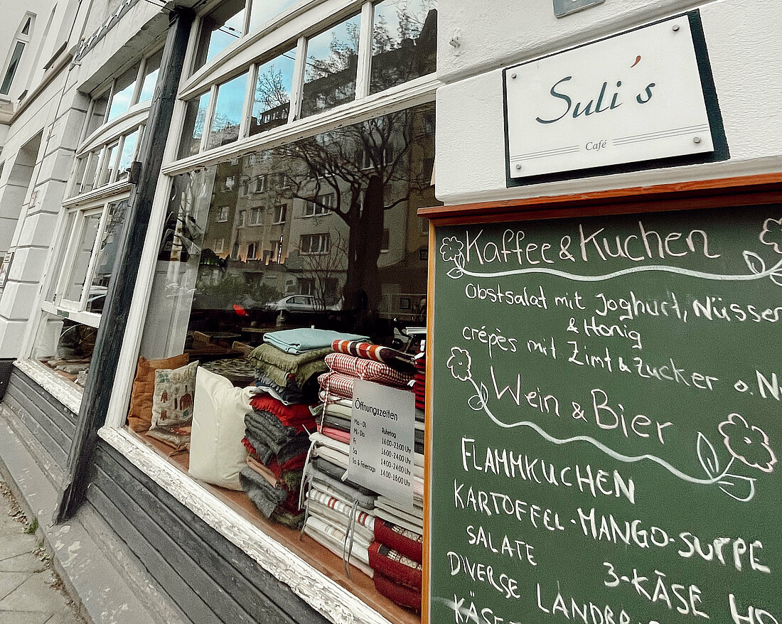 Im Suli's kann man sowohl Kaffee als auch Wein genießen. (Foto: Mia Hellbeck) Es ist die Hauswand des Cafe Sulis mit Fokus auf das dort angebrachte Namensschild und der Menü-Tafel zu sehen.