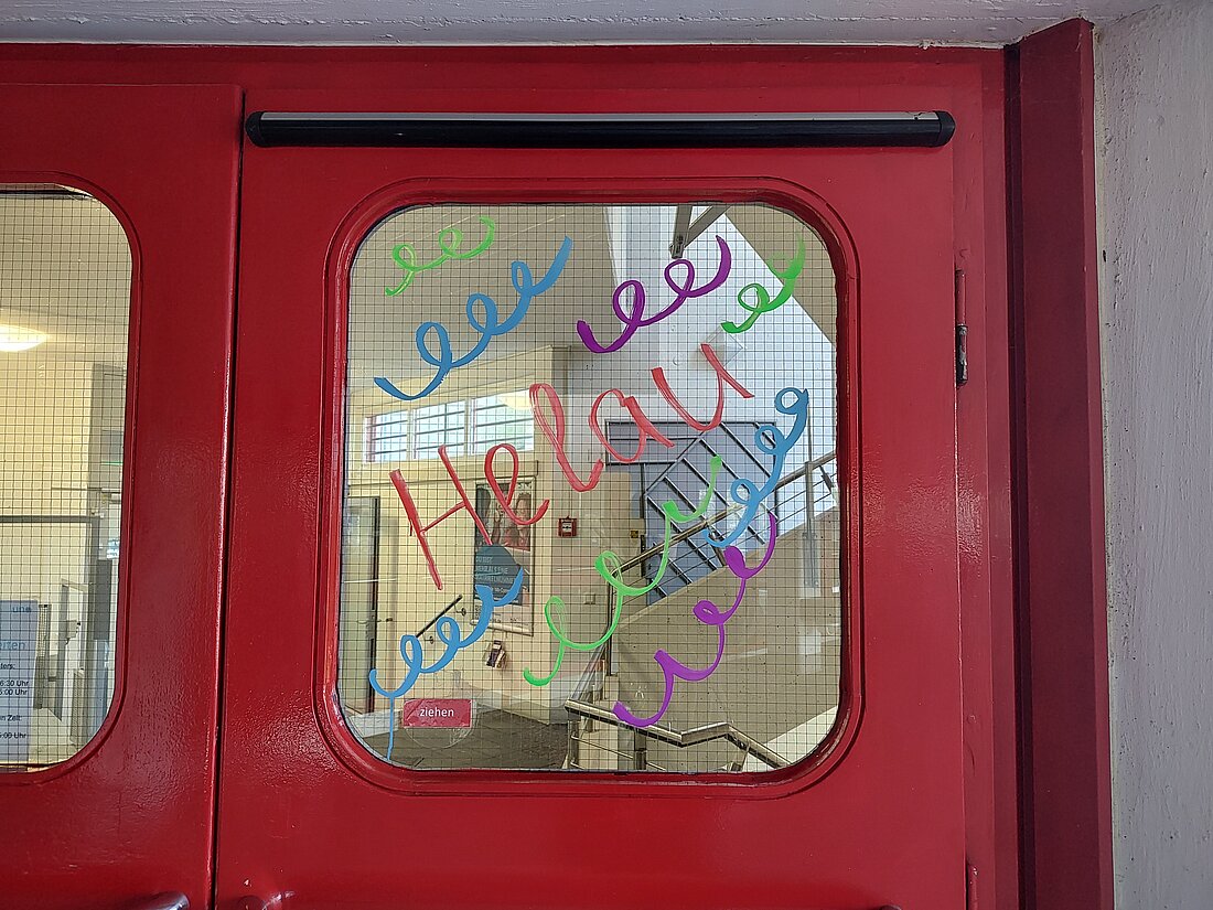"Helau" in bunter Schrift auf einer der roten Mensa Türenfenster der Heinrich Heine Universität.