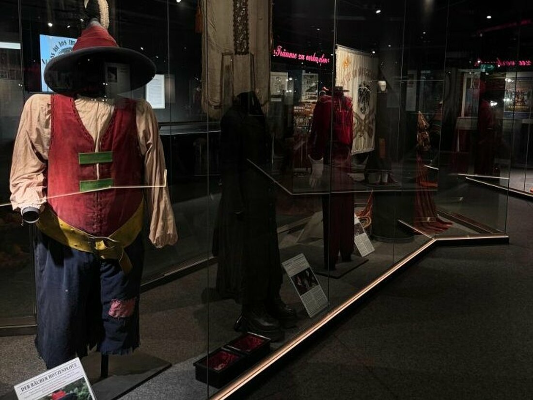Auf dem Bild sind bunte Kostüme in einer beleuchteten Glasvitrine zu sehen.