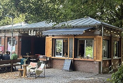 Man sieht ein kleines Café mit Sitzgelegenheiten im Grünen