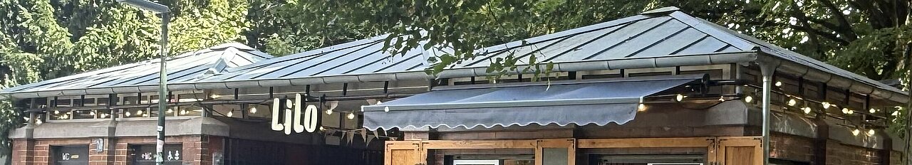 Man sieht ein kleines Gebäude, dass im Schatten der Bäume steht und sich direkt an einem Bach befindet 