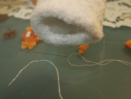 Eine offene mit Füllwatte gefüllte Socke und eine Nadel durch die weißes Garn gezogen ist.