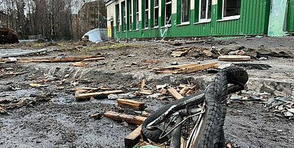 Man sieht im Vordergrund ein kaputtes Fahrrad und ein heruntergekommenes grünes Gebäude im Hintergrund.