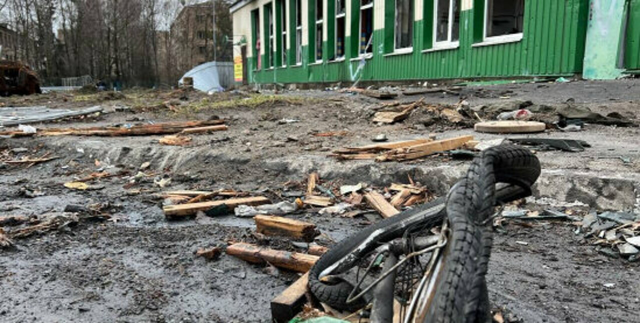 Man sieht im Vordergrund ein kaputtes Fahrrad und ein heruntergekommenes grünes Gebäude im Hintergrund.