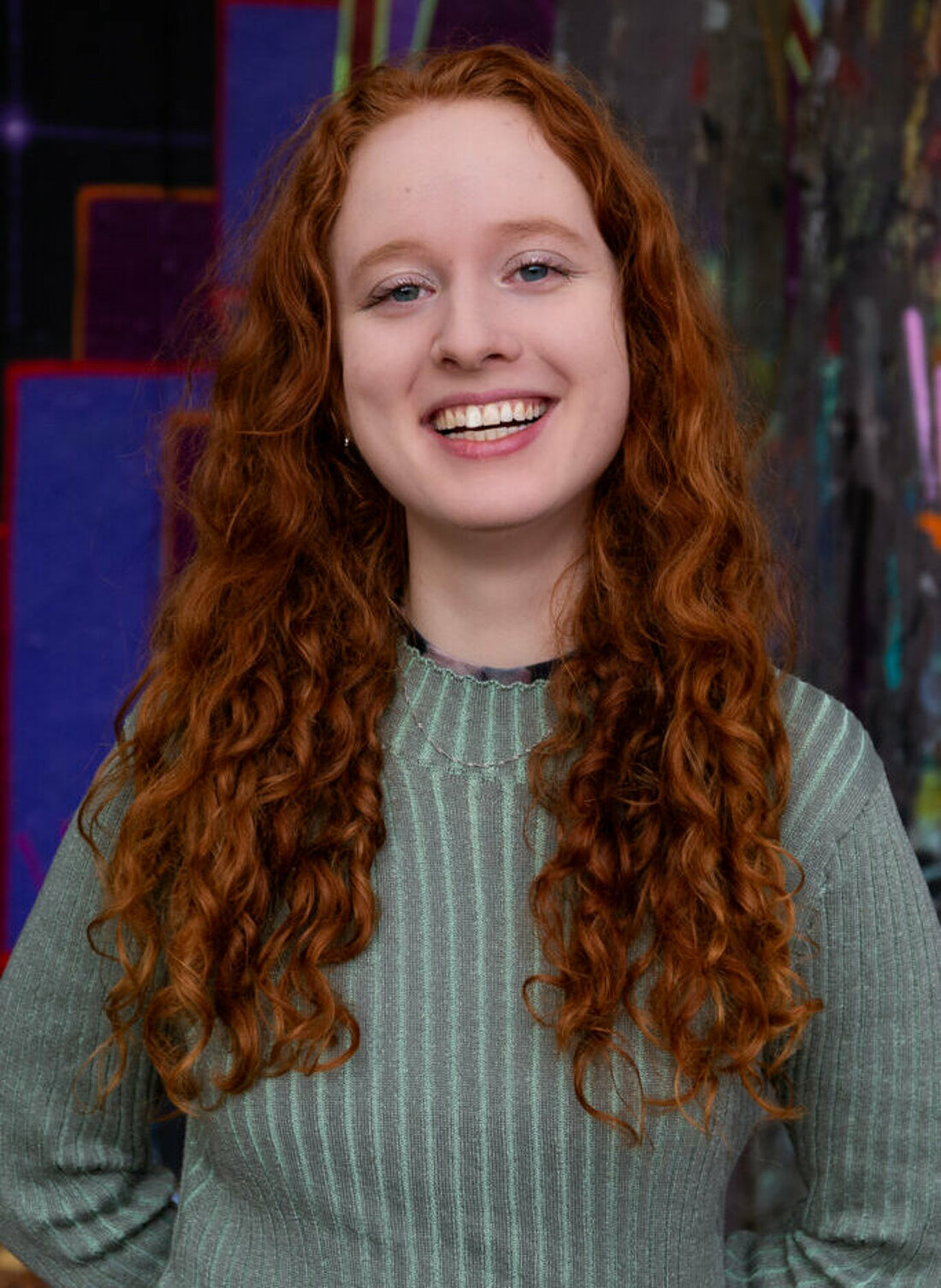 Das Bild zeigt das Vorstandsmitglied des fzs, Katharina Rummenhöller lächelnd in grünem Pullover vor blauem Hintergrund.