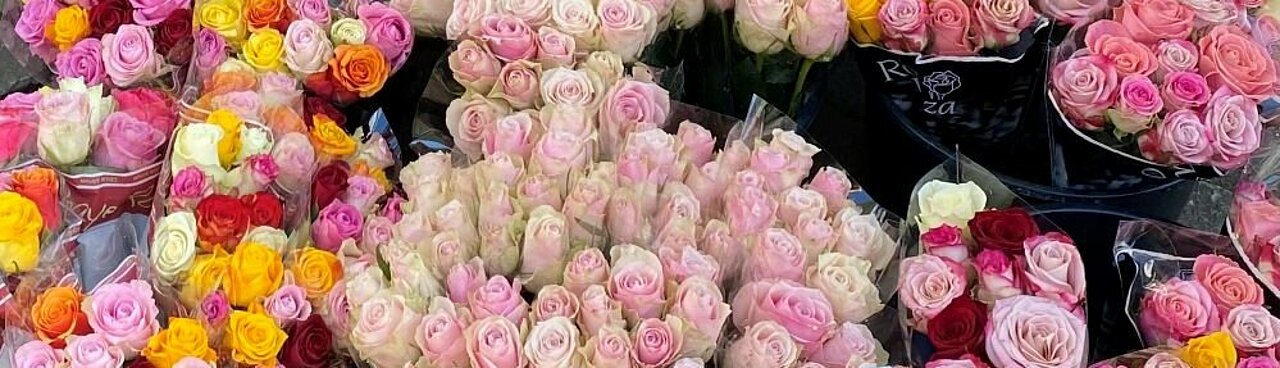 Auf dem Foto sind Blumensträuße vor einem Blumenladen zu sehen. Vorne sind mehrere rosane Rosen. In der Mitte der Blumensträuße steckt ein weißes Preisschild.