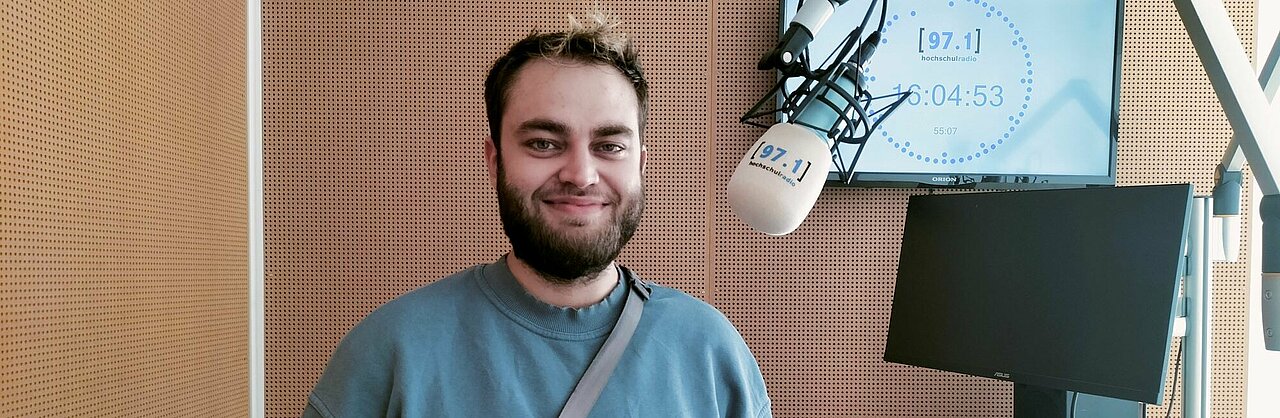 Auf dem Foto ist Elias Warnke zu sehen. Er steht neben einem Mikrofon und lächelt in die Kamera.