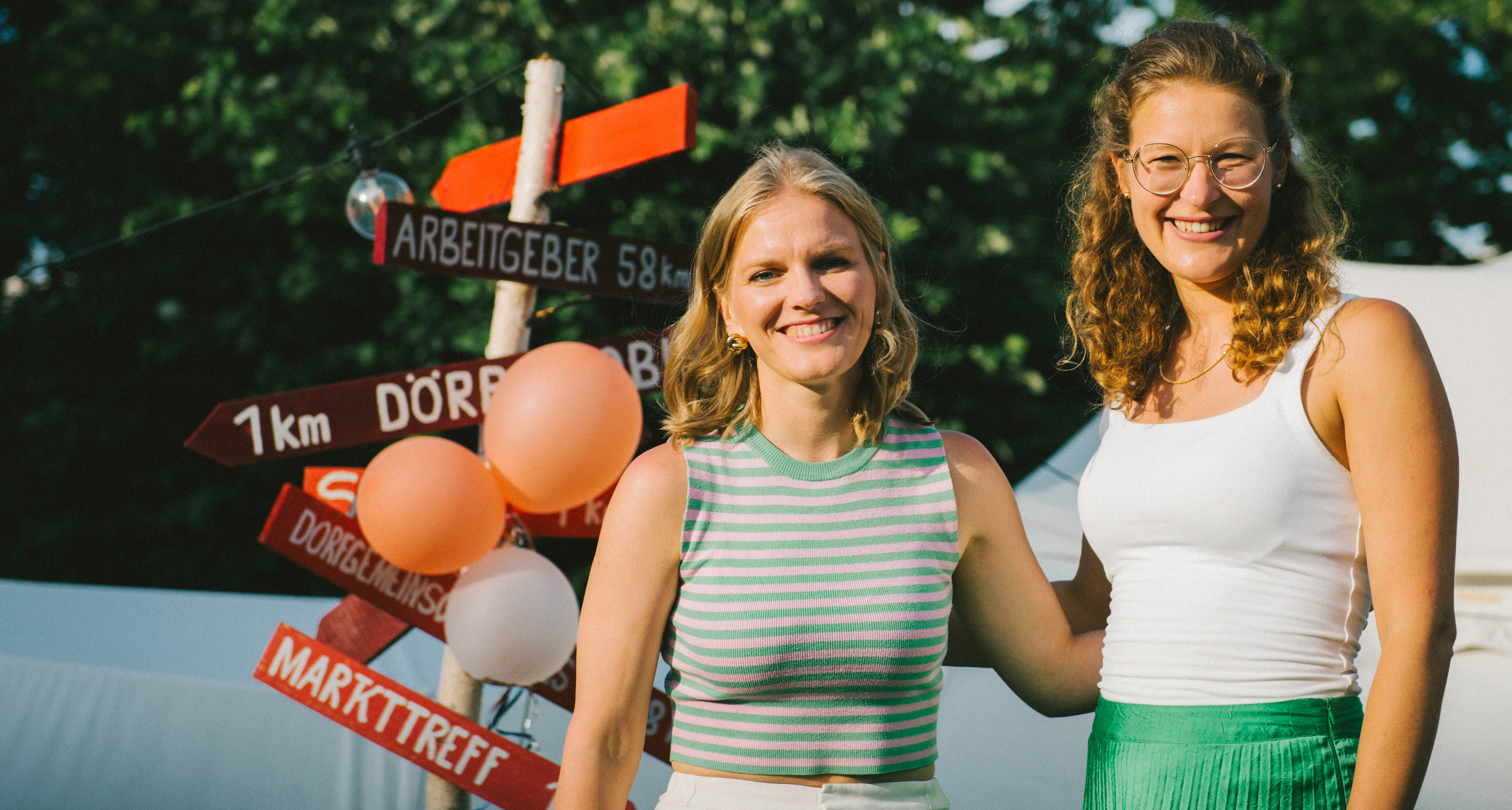 Auf dem Foto sind Isabell Nethke und Julia Riensche zu sehen. Sie stehen vor einem roten Schild und lächeln in die Kamera.