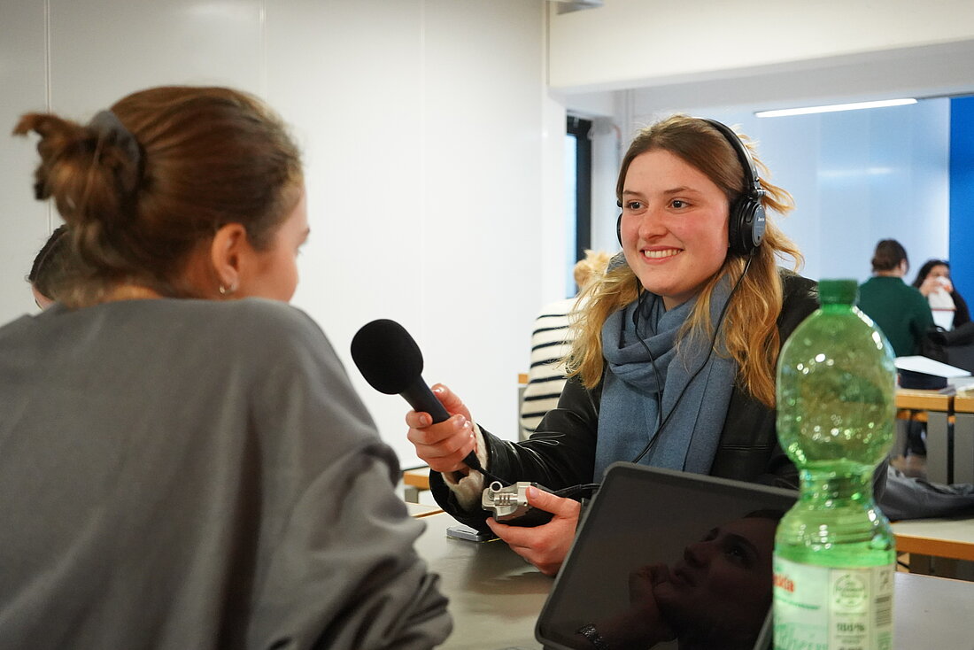 hochschulradio-Redakteurin Antonia Müller hält ein Mikrofon und spricht mit Larissa (von hinten zu sehen), einer weiteren Studentin der HHU.