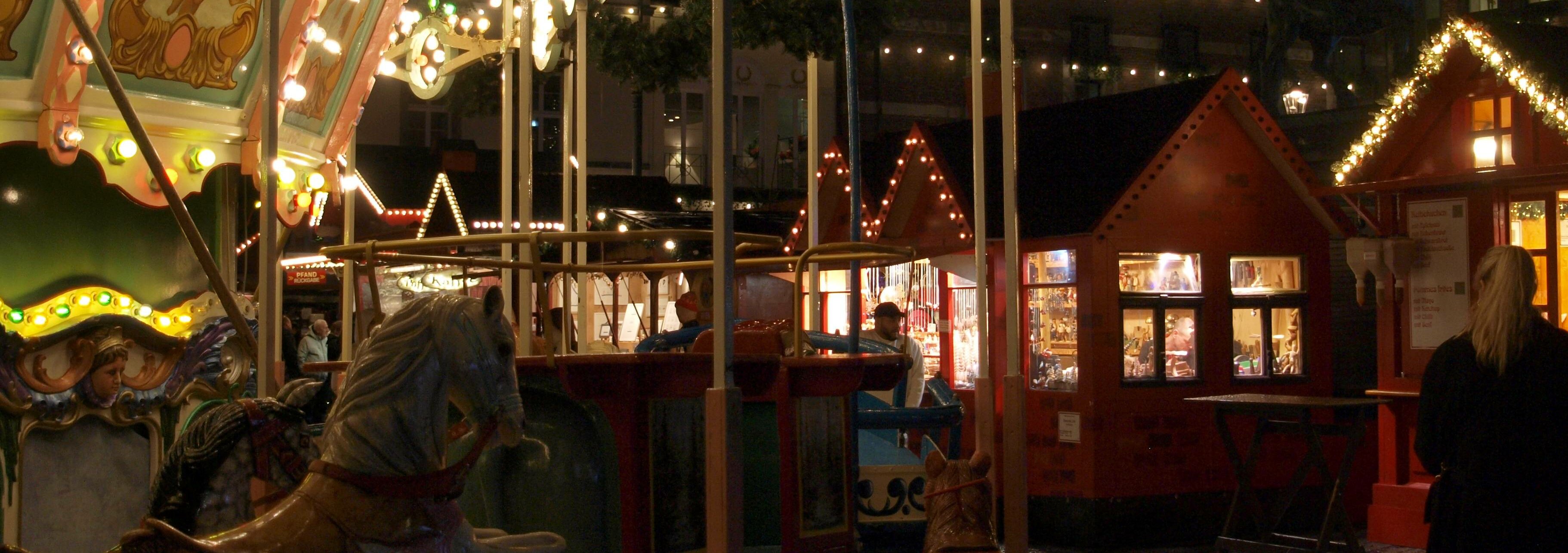 Ein Kinderkarussel auf einem Weihnachtsmarkt mit roten Häuschen vor dem Düsseldorfer Rathaus.