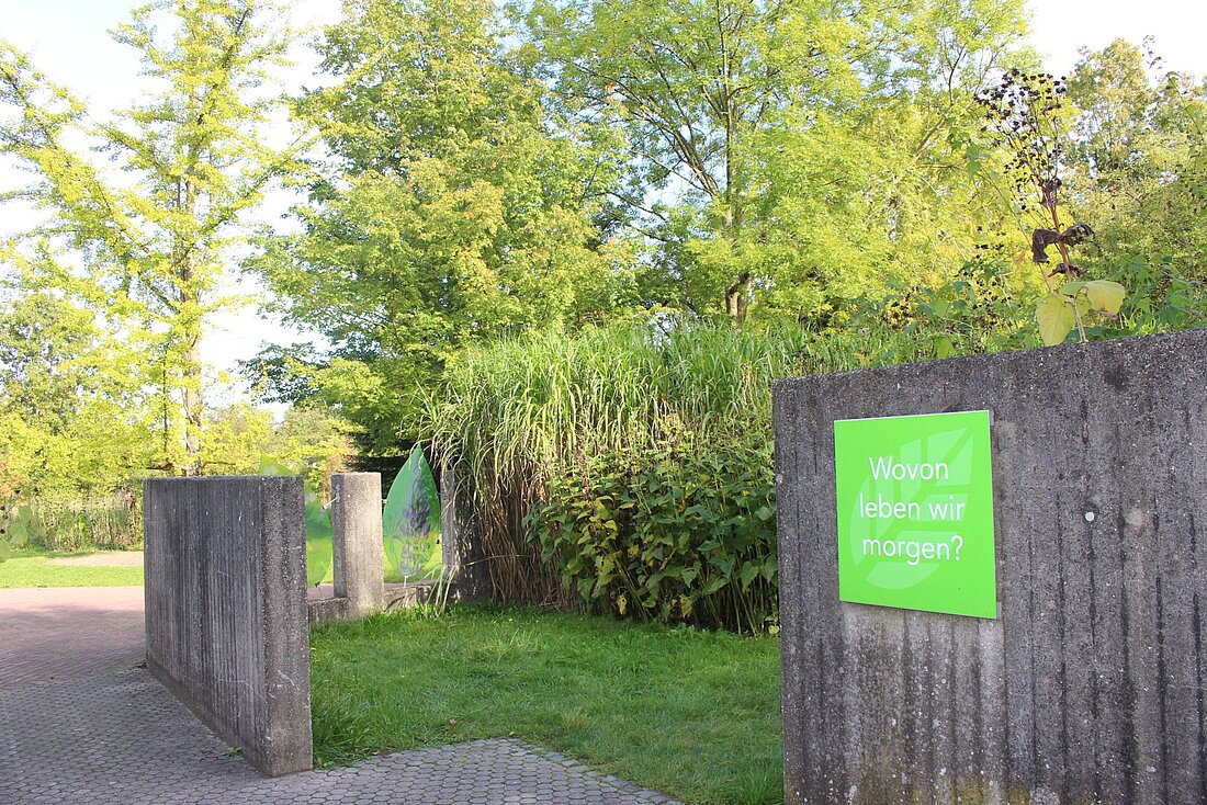 Ein Schild mit der Frage "Wovon leben wir morgen?" am Eingang zu einem Gartenabschnitt.