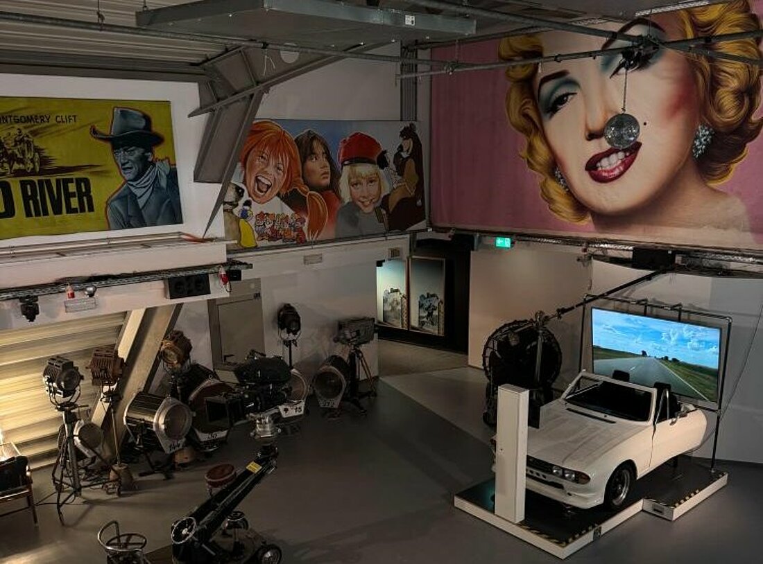 Auf dem Bild sieht man einen Studioraum gefüllt mit Kameras, einer Windmaschine und Beleuchtungsanlagen. Die Wände sind verziert mit einer großen Flagge der Schauspielerin Marylin Monroe und weiteren Filmfiguren, wie Pippi Langstrumpf.