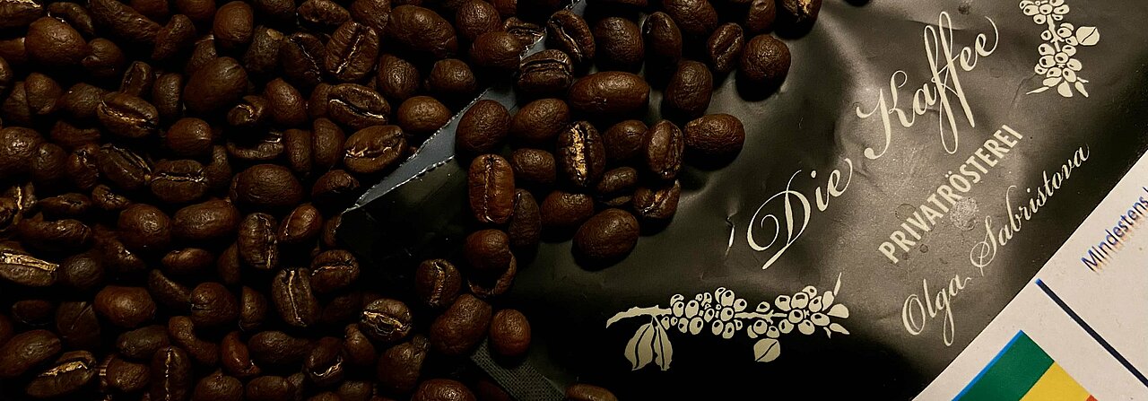 Auf dem Bild sieht man eine Kaffeeverpackung aus der Die-Kaffee-Rösterei mit gerösteten Kaffeebohnen.