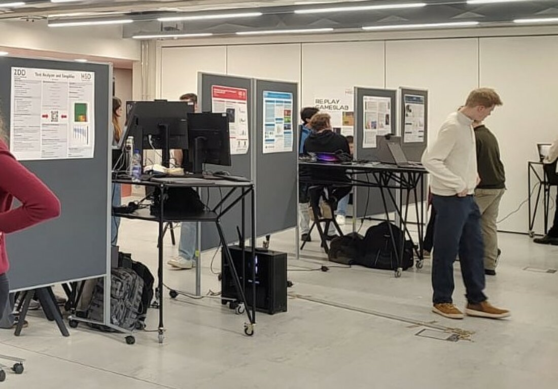 Ein Raum in welchem Plakate an Wänden hängen und Menschen neben diesen stehen.