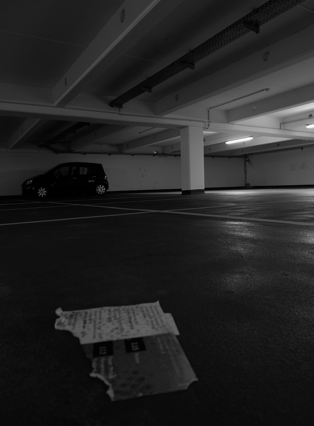 Ein einzelnes Auto in einem Parkhaus der Uni und auf dem Boden liegt ein zerrissener Flyer der Campus Security.