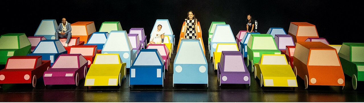 Die Klimakrise spaltet in dem Theaterstück die Generationen (Foto: Sandra Then). Auf dem Bild sind Glenn Goltz, Charlie Schrein, Claudia Hübbecker und Cennet Rüya Voß, wie sie auf den bunten Pappautos des Bühnenbilds sitzen.
