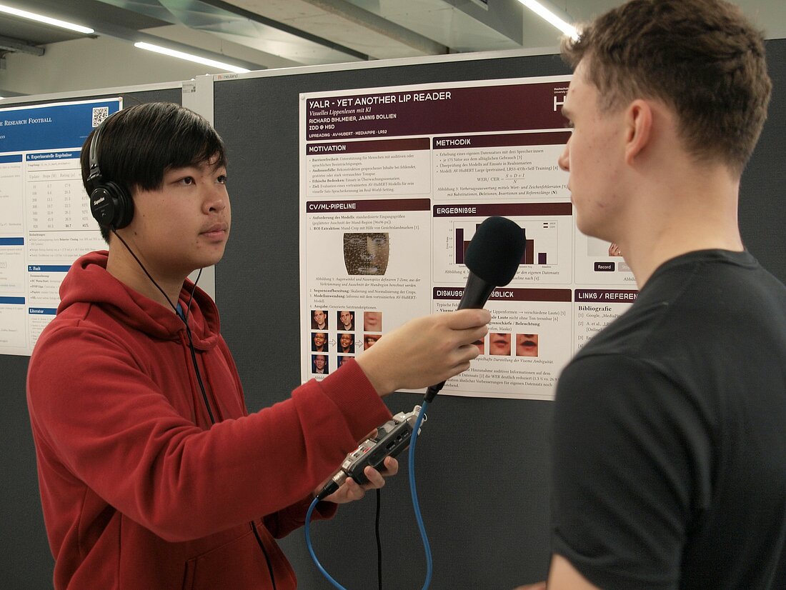 Ein Mann interviewed einen anderen Mann vor einem Plakat über das Thema Lippenlesen.