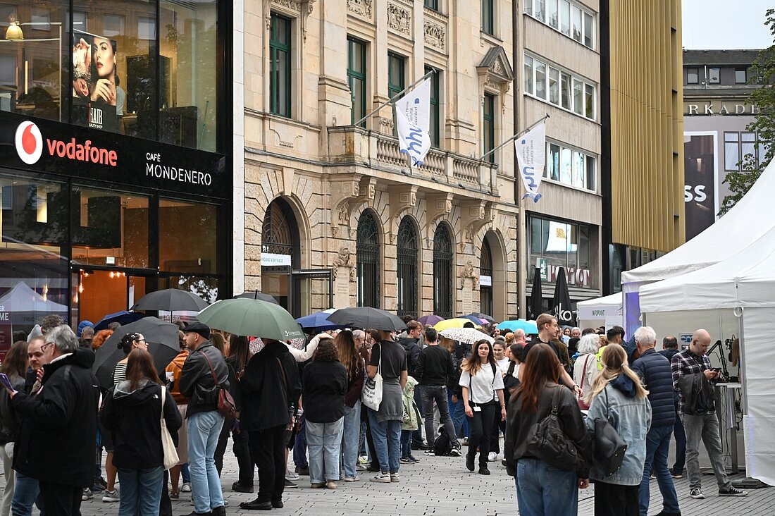Man sieht eine Schlange von Menschen, die Regenschirme haltend vor dem Haus der Universität warten.