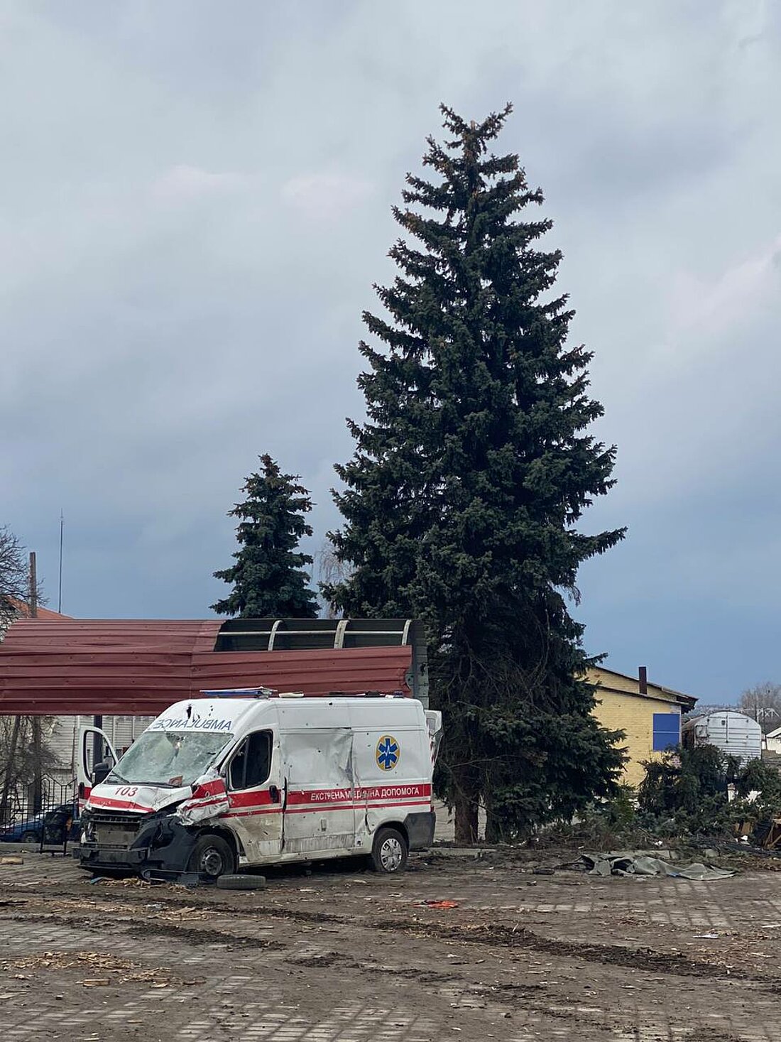 Man sieht einen demolierten ukrainischen Krankenwagen, der am Rand eines Platzes steht.