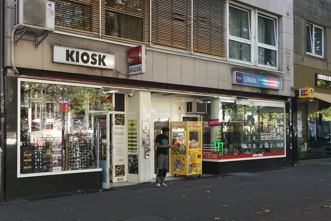 Eine weitere Fassade eines Kiosks an der Heinrich-Heine-Allee. Davor steht ein Mann und schaut auf sein Handy.