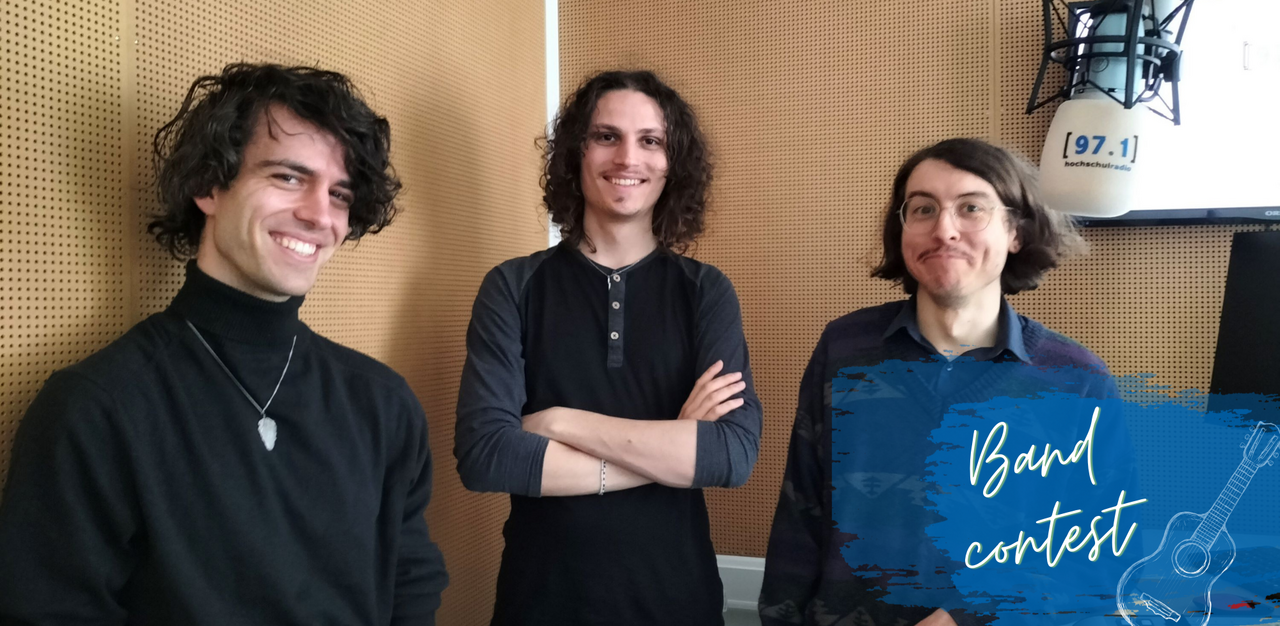 Auf dem Foto sind drei Mitglieder der Band Discoville zu sehen. Sie stehen nebeneinander und lächeln in die Kamera. Ganz rechts ist ein weißes Mikrofon mit dem Logo von hochschulradio düsseldorf im Bild.
