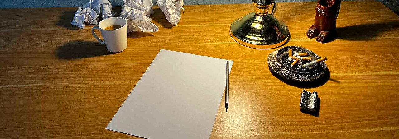 Auf dem Bild sieht man einen Schreibtisch mit einem Papier, einer Lampe und Zigaretten drauf. In der Ecke steht noch eine Tasse Kaffee (Foto: Gregory Sheftel) 