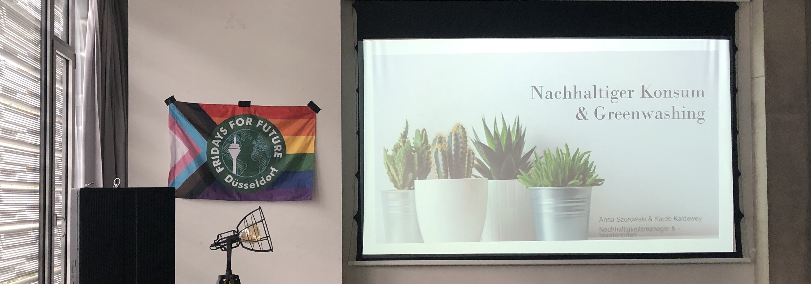 Die Public Climate School in den Räumen der HSD (Foto: Valeska Ridzewski) Eine Prideflagge von den Students for Future steht neben dem Beamer auf dem "Nachhaltiger Konsum und Greenwashing" steht.