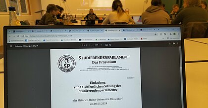 Die Einladung zur SP-Sitzung. Im Hintergrund sind die Mitglieder des SPs zu sehen.