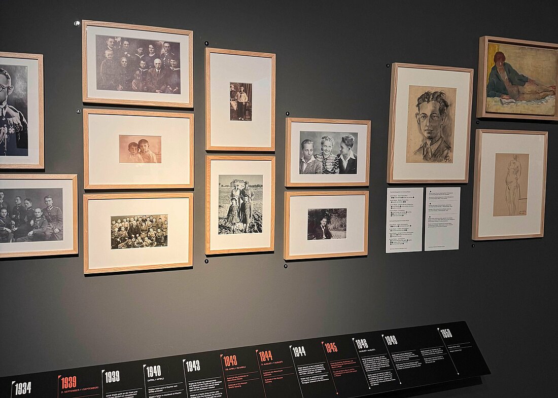 Auf dem Bild sieht man eine Wand gefüllt von mehreren Bilderrahmen, in denen Fotos, Skizzen und Zeichnungen des Regisseurs Andrzej Wajda zu sehen sind. Ergänzt werden die Bilderrahmen von Zitaten des Regisseurs und einem Zeitstrahl mit Jahreszahlen, die die Meilensteine seines Lebenswerks vertieft erklären.