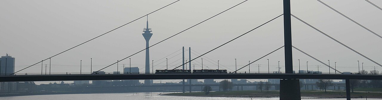 Auf dem Bild sieht man die  Rheinkniebrücke und den Fernsehturm in Düsseldorf. Über die Brücke fährt eine Ubahn.