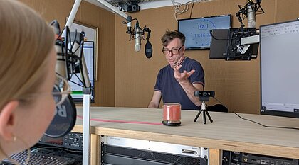 Auf dem Bild sieht man Moderatorin Hannah Vogel im Gespräch mit Christian Uffmann. Die beiden stehen in einem Radiostudio.