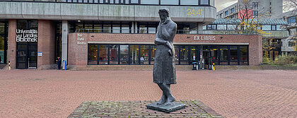 Die Heine-Statue mit der Universitäts- und Landesbibliothek und dem Café „Ex Libris“ im Hintergrund.