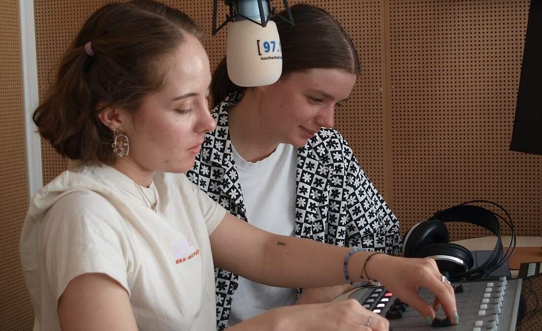 Zwei Personen stehen im Tonstudio und bedienen ein Mischpult.