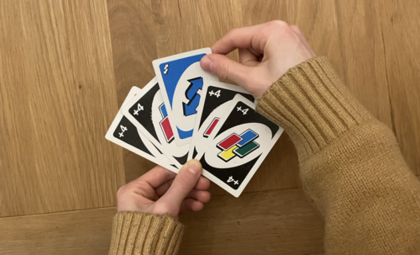 Auf dem Bild sieht man eine Hand, die Uno-Karten hält und eine Richtungswechel-Karte nimmt. 
