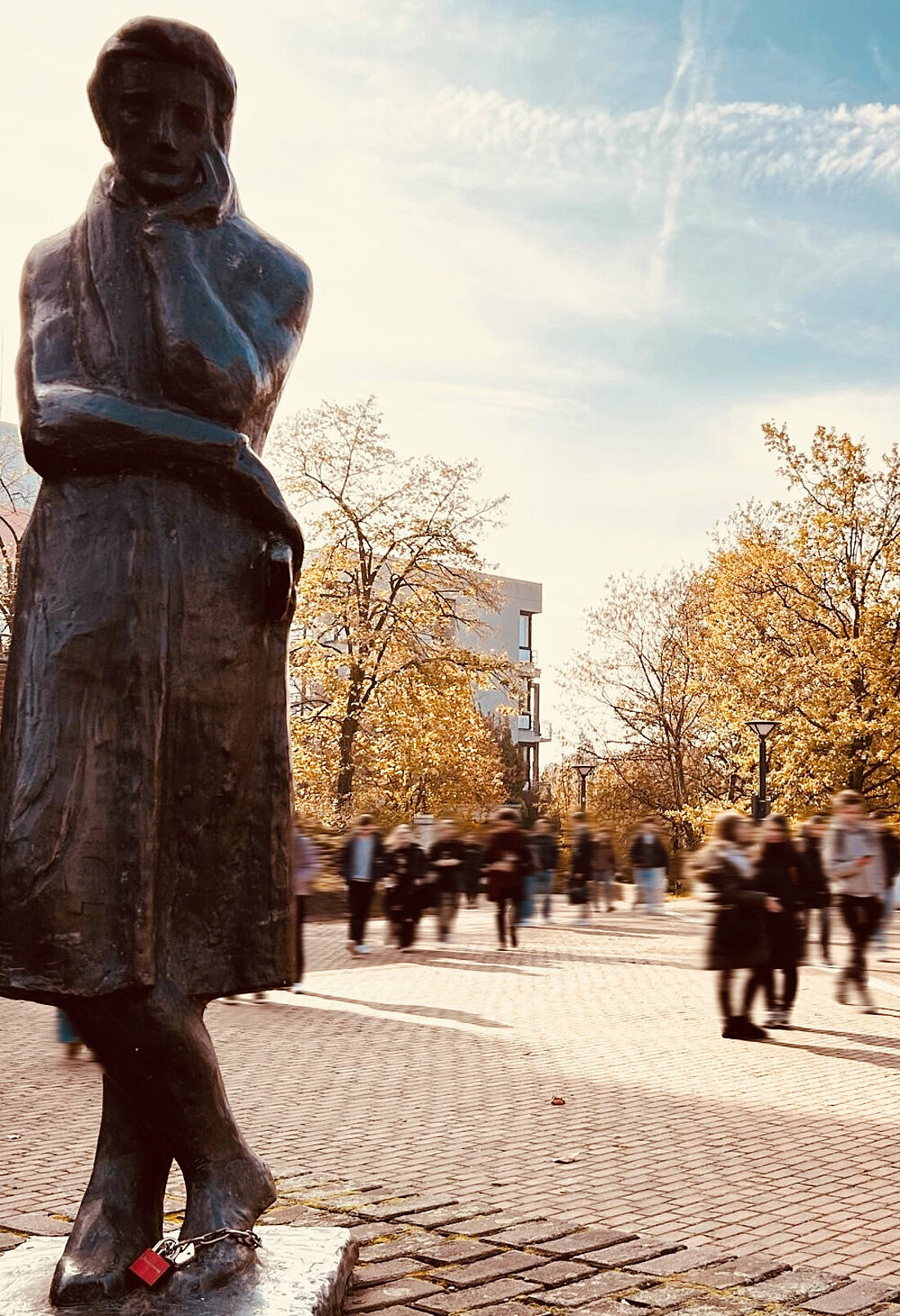 Die Heinrich Heine Statue auf der linken Seite im Fokus mit einem Liebesschloss am Fuß.
